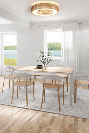 A Kilimanjaro wicker ceiling fan with integrated LED light. It is above a wooden dining table surrounded by six chairs. The decor is traditional and pale.